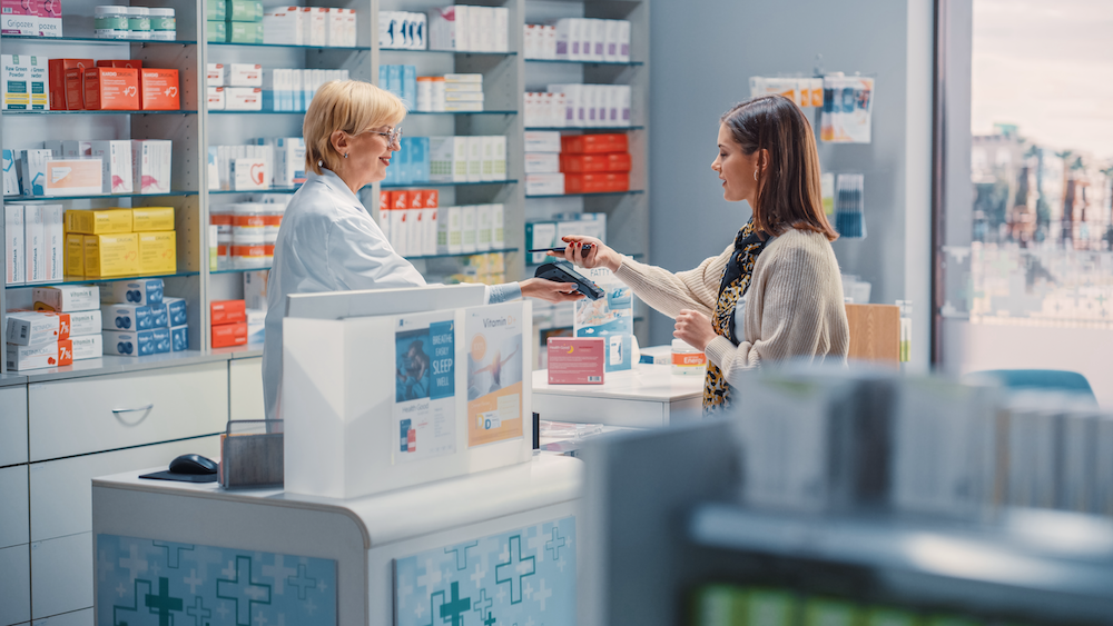 Photo of a woman checking out at a pharmacy using tap-to-pay on her phone, highlighting specialty audience research in healthcare.