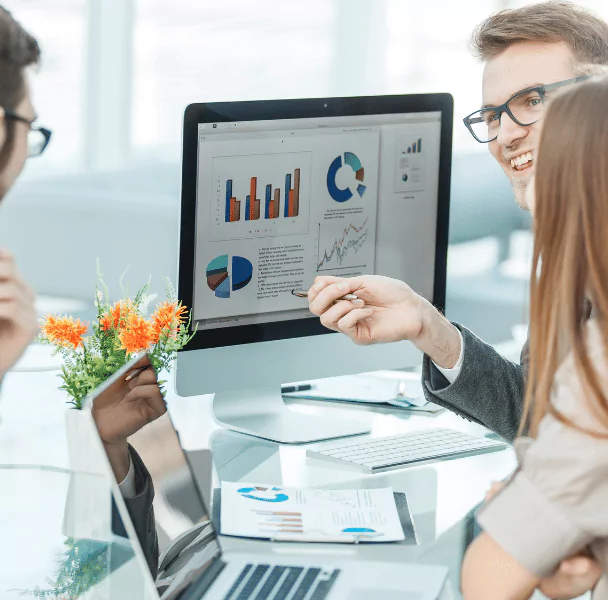 Three people sitting at a desk reviewing sample market sizing reports on a computer, analyzing data for growth opportunities and market segmentation.